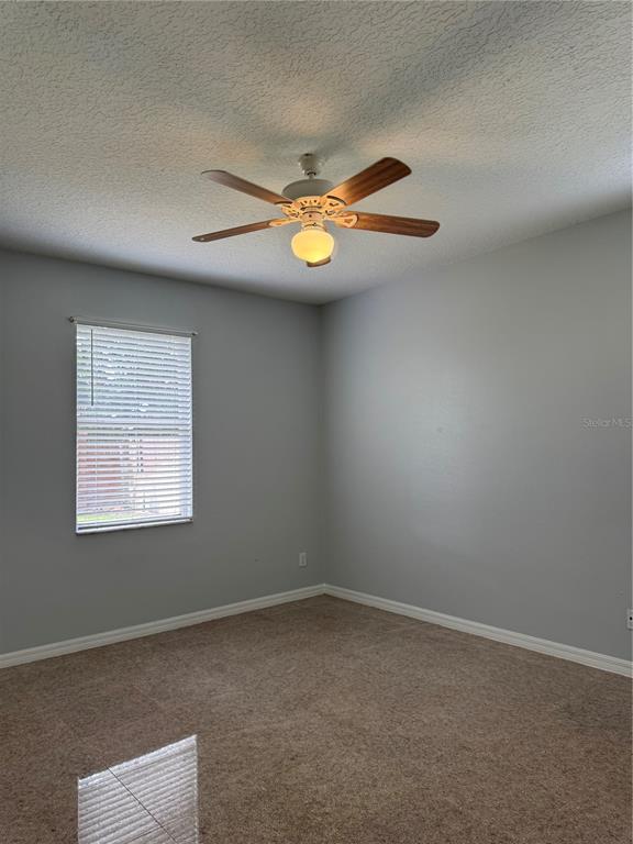 An empty bedroom features light gray walls, beige carpeting, and a ceiling fan with light — 1767 CAMBRIDGE VILLAGE COURT, OCOEE, FL