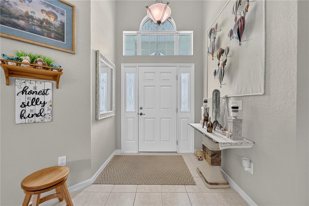 An entryway features a white front door, tile flooring, a console table, and wall decor — 11042 SW 73RD COURT, OCALA, FL