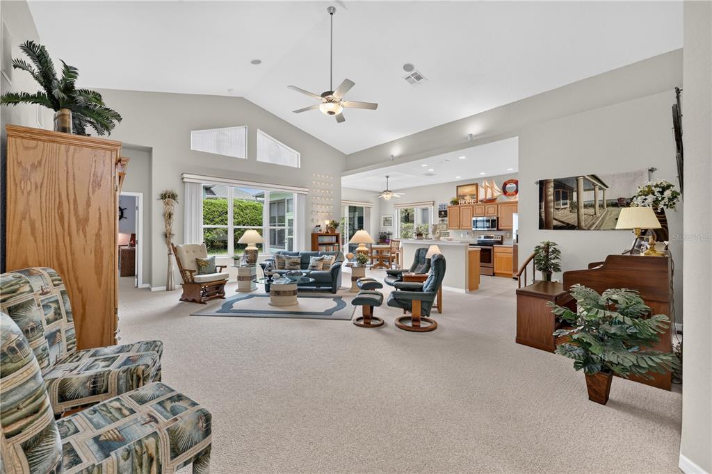 A spacious living room with vaulted ceilings, carpeted floors, and an open-concept kitchen beyond — 11042 SW 73RD COURT, OCALA, FL