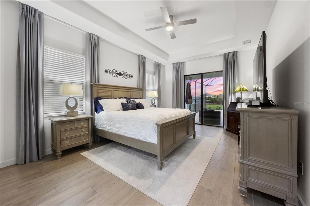 A bedroom features a king bed, wood-look flooring, a ceiling fan, and sliding glass doors — 15306 GOLDEN BEAM PLACE, BRADENTON, FL
