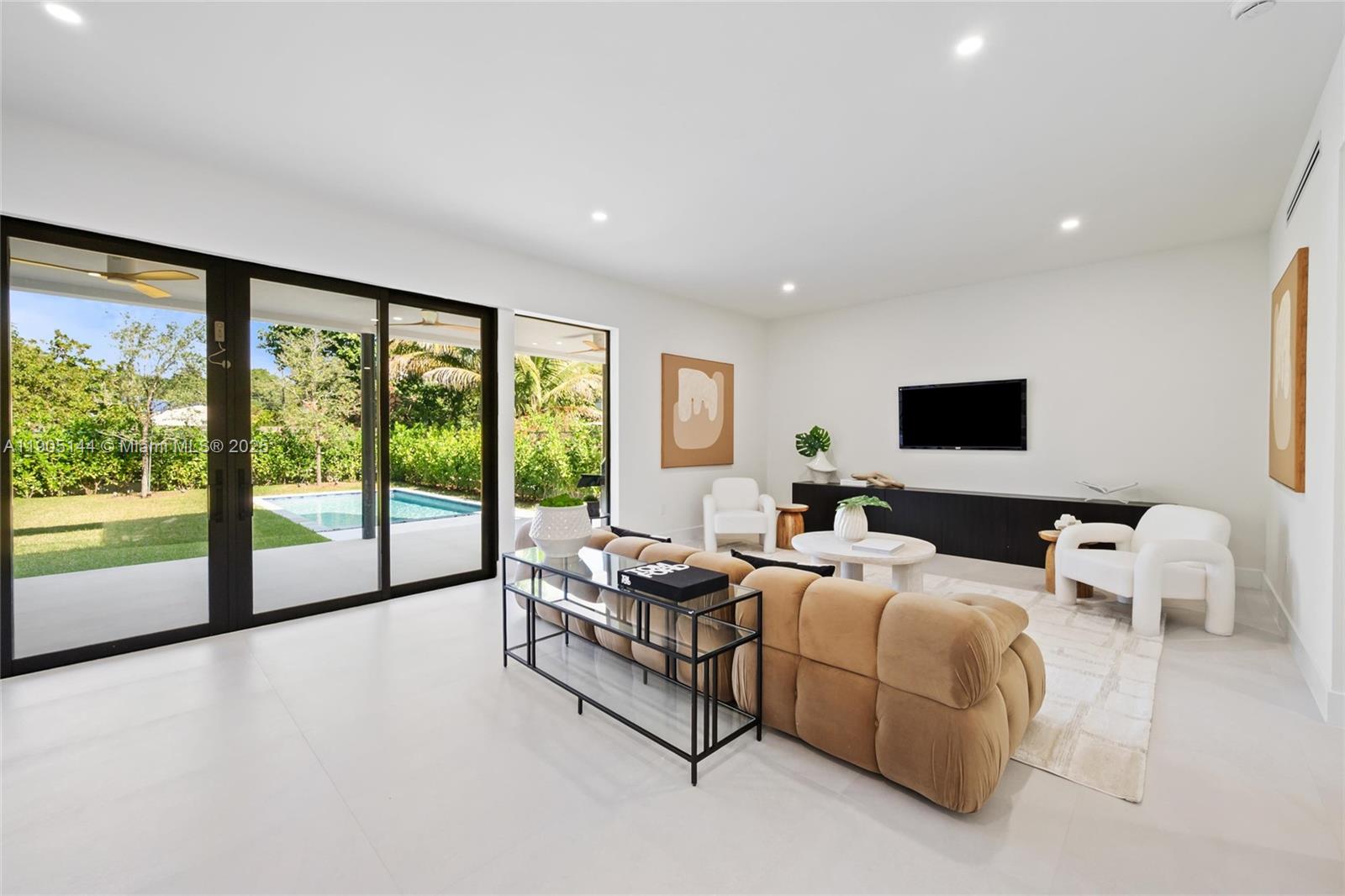 A modern living room features a tan sofa, white armchairs, and sliding doors overlooking a pool — 2127 SW 11th Ter, Miami FL 33135, MIAMI, FL