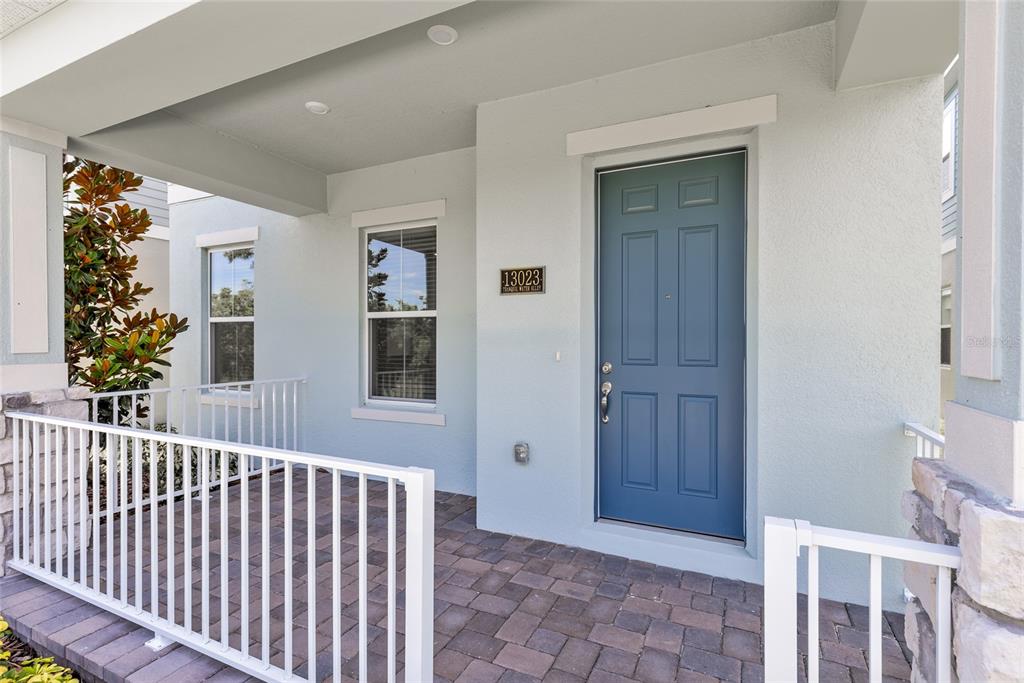 A covered front porch with a blue door, white railings, and stone accents — 13023 TRANQUIL WATER ALLEY, WINTER GARDEN, FL