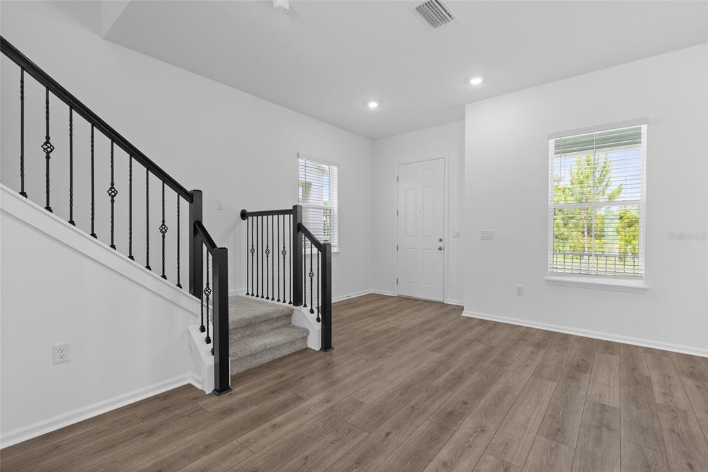 An entryway with wood-look flooring, a carpeted staircase with black railings, and a white door — 13023 TRANQUIL WATER ALLEY, WINTER GARDEN, FL