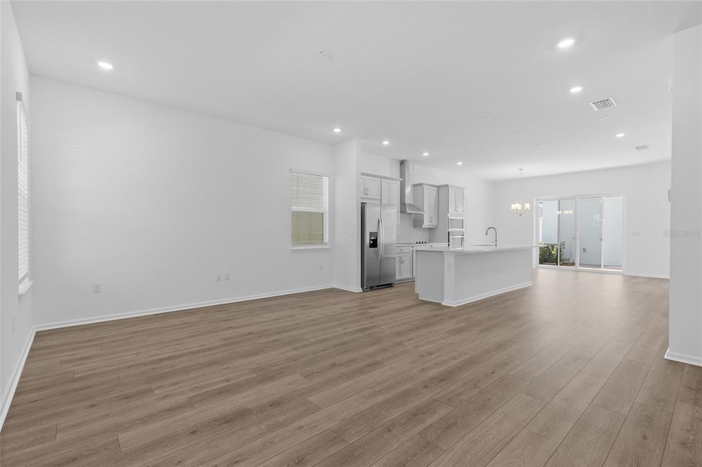 An open-concept kitchen and living area features white cabinetry, a center island, and wood-look flooring — 13023 TRANQUIL WATER ALLEY, WINTER GARDEN, FL