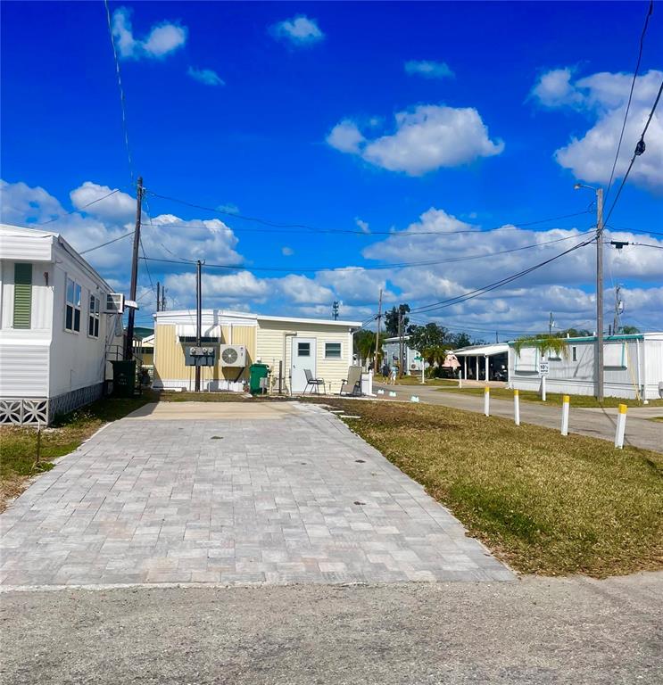 A paved driveway leads to a yellow mobile home under a bright blue sky — 167 4TH STREET W, PALMETTO, FL