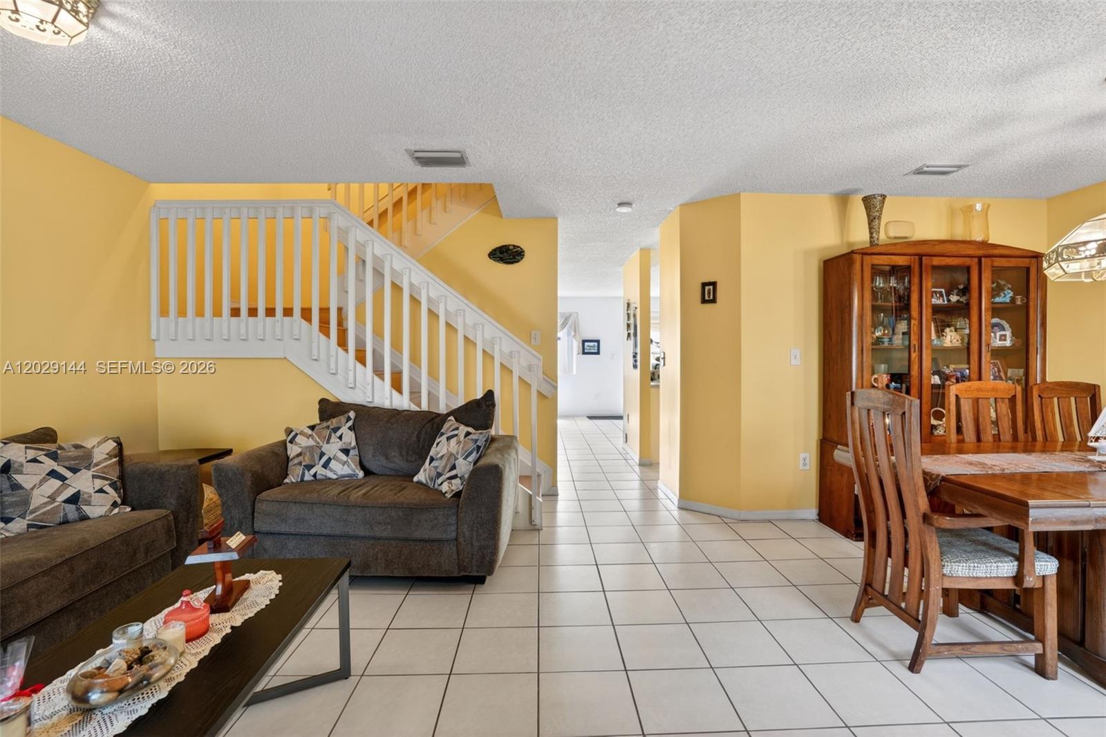 A living and dining area features yellow walls, white tile floors, and a wooden staircase — 9633 SW 163rd Ct, Miami FL 33196, MIAMI, FL