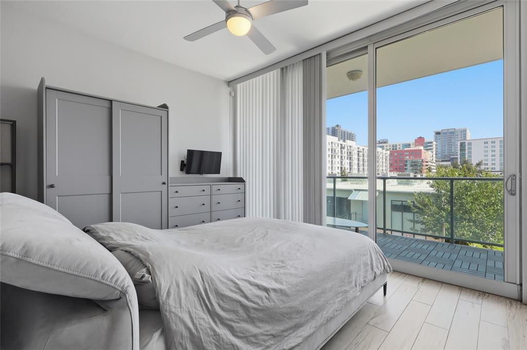 A bedroom features a gray wardrobe, a dresser with a wall-mounted television, and a balcony — 111 N 12TH STREET UNIT 1310, TAMPA, FL