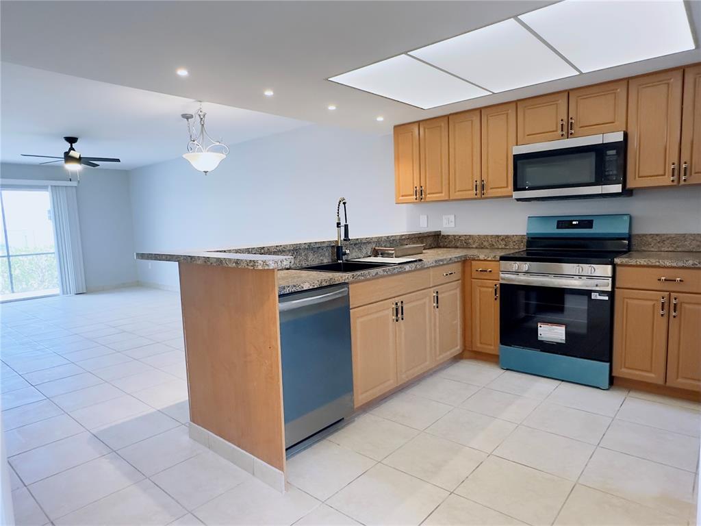 A kitchen with light wood cabinets, granite countertops, and stainless steel appliances overlooks a living area — 6800 PLACIDA ROAD UNIT 179, ENGLEWOOD, FL