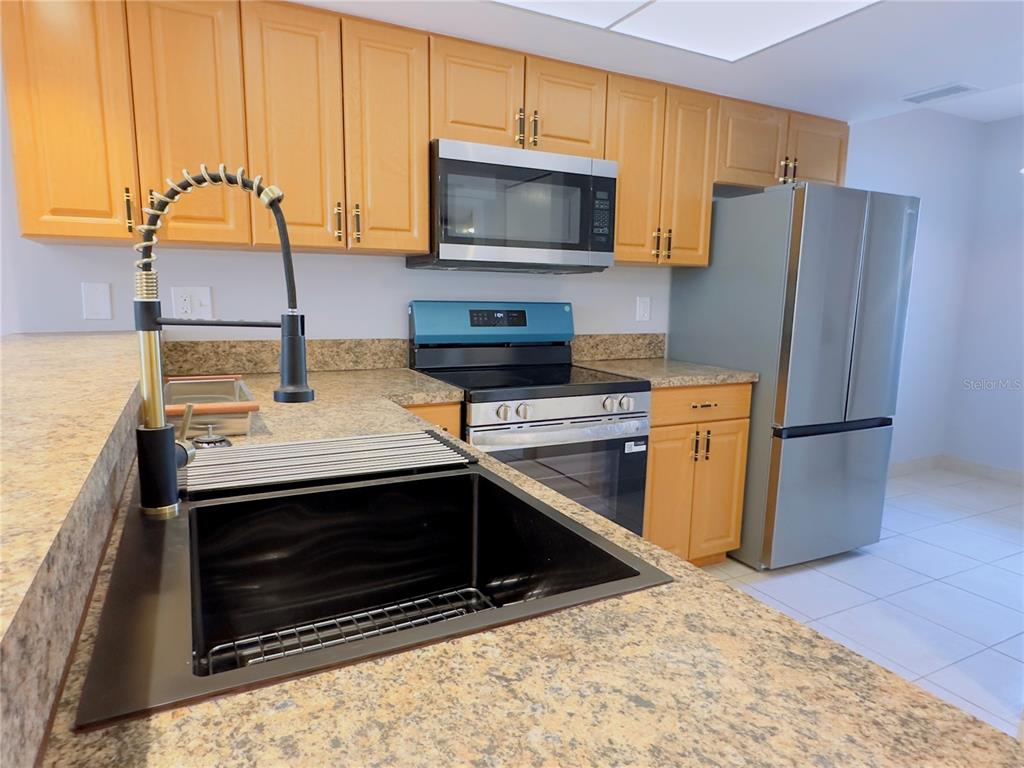 A kitchen features light wood cabinets, granite countertops, stainless steel appliances, and a black sink — 6800 PLACIDA ROAD UNIT 179, ENGLEWOOD, FL