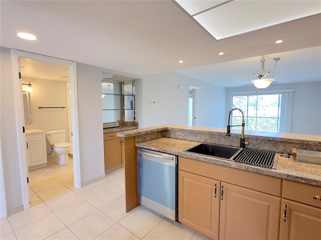 A kitchen with light wood cabinets, granite countertops, and a dishwasher overlooks a living area — 6800 PLACIDA ROAD UNIT 179, ENGLEWOOD, FL