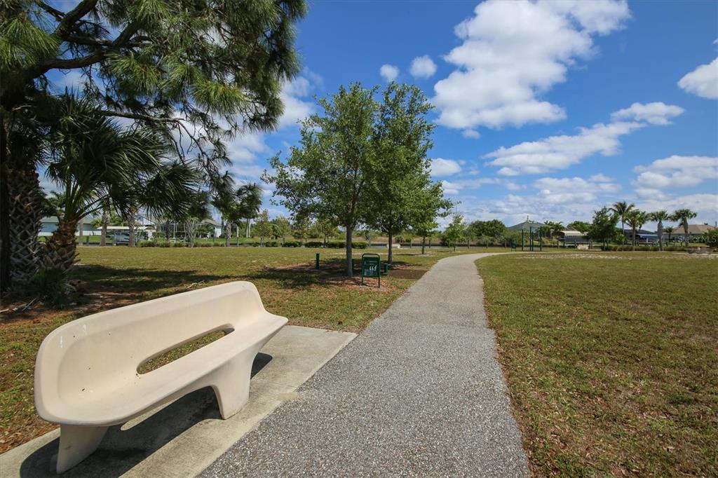 A paved walking path winds through a grassy park with a bench and several trees — 13305 BLAKE DRIVE, PORT CHARLOTTE, FL