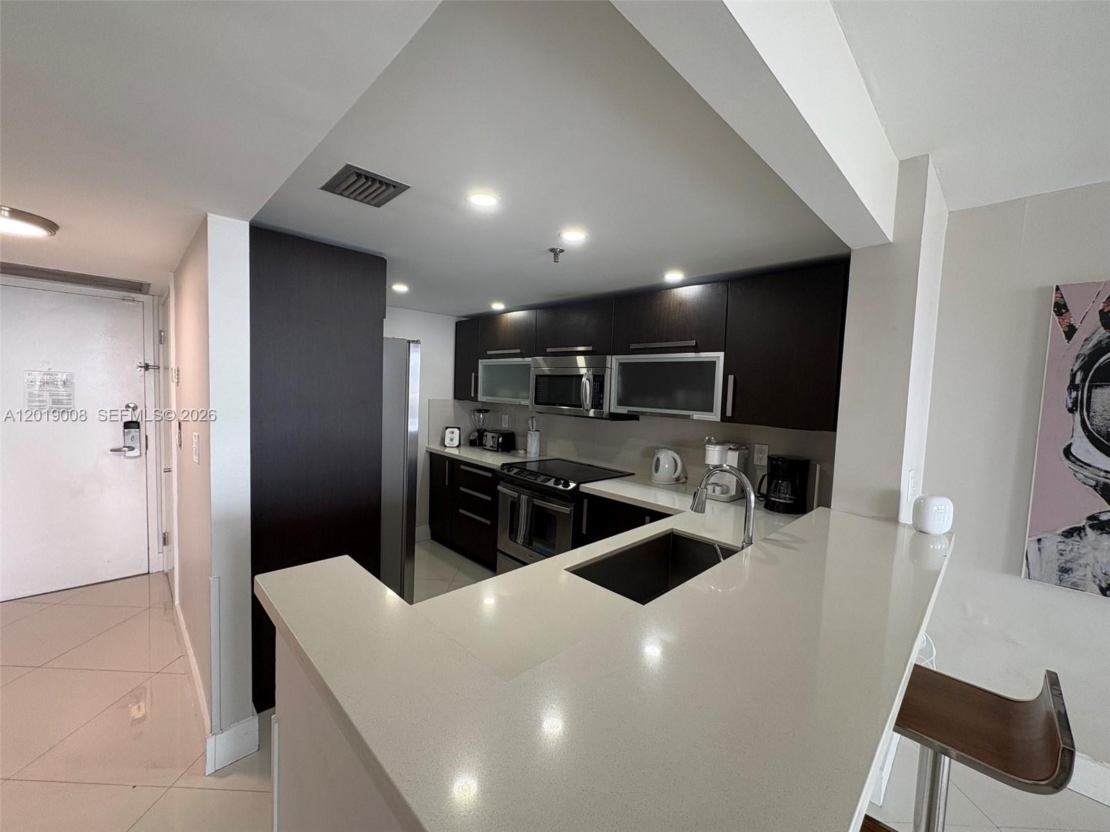 A modern kitchen features dark wood cabinets, stainless steel appliances, and a white quartz countertop — 1717 N Bayshore Dr # 2054, Miami FL 33132, MIAMI, FL