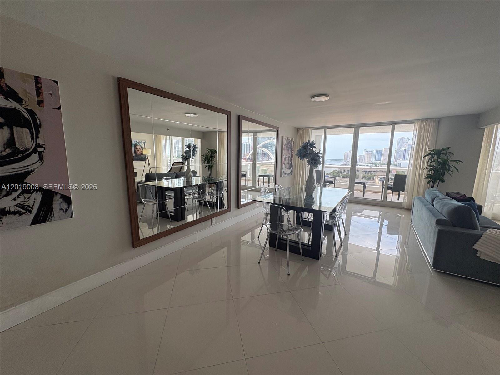 A dining area features a glass table, transparent chairs, large wall mirrors, and tile flooring — 1717 N Bayshore Dr # 2054, Miami FL 33132, MIAMI, FL