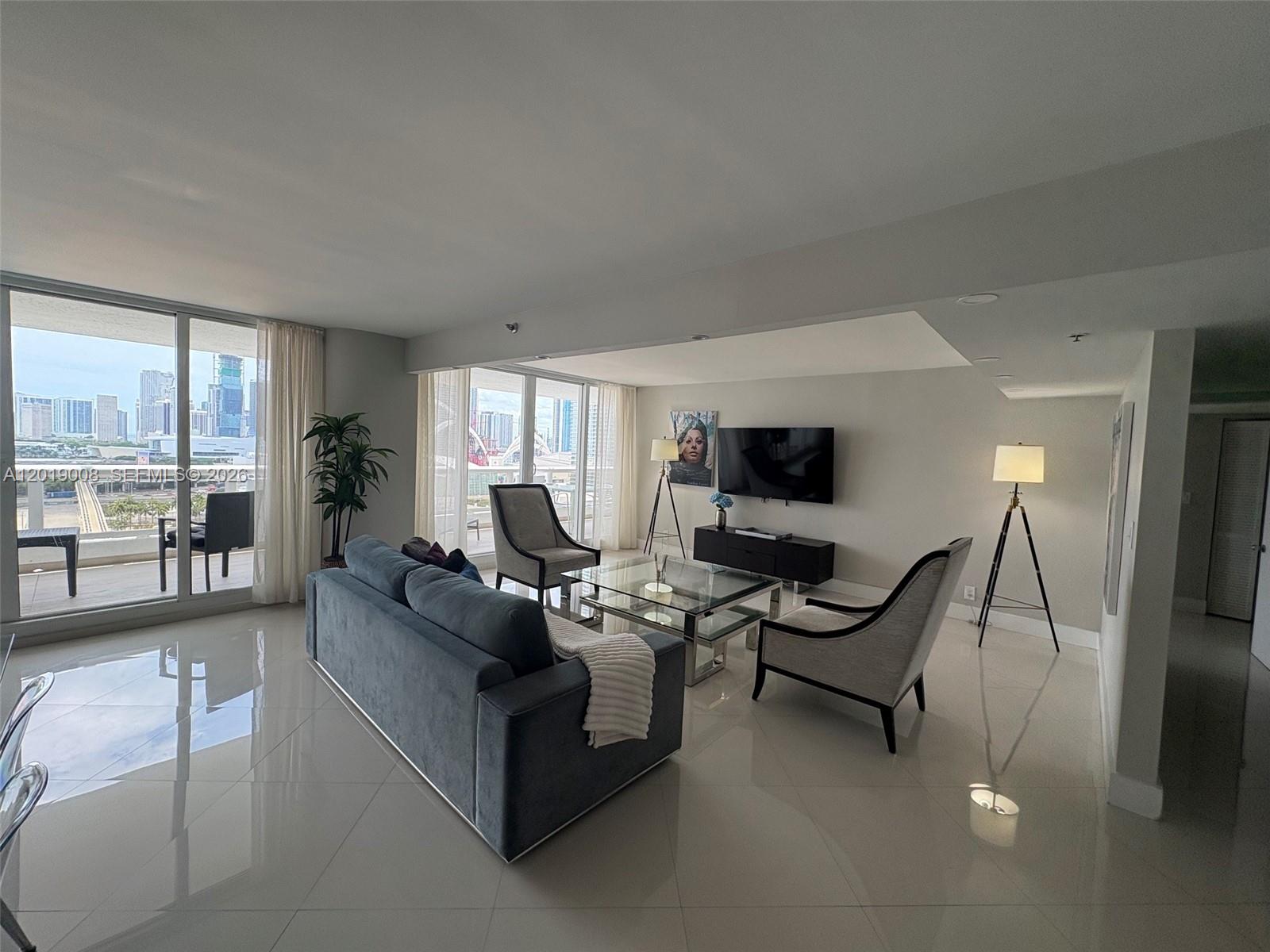 A modern living room features a blue sofa, glass coffee table, and floor-to-ceiling windows — 1717 N Bayshore Dr # 2054, Miami FL 33132, MIAMI, FL