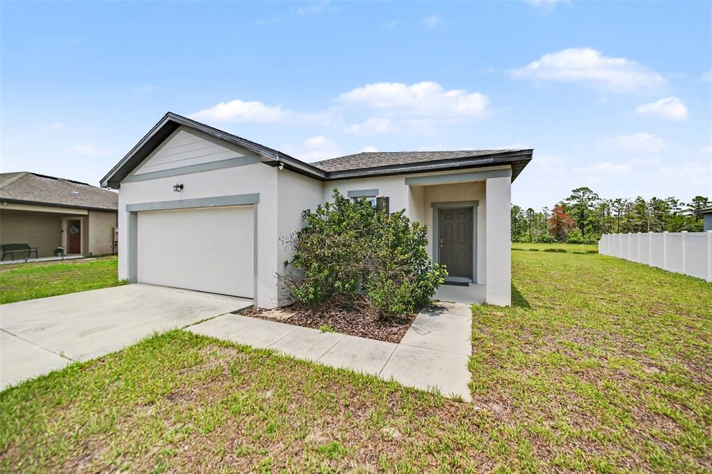 A single-story house with a white stucco exterior, a two-car garage, and a front lawn — 1006 COMMUTER DR, DELTONA, FL