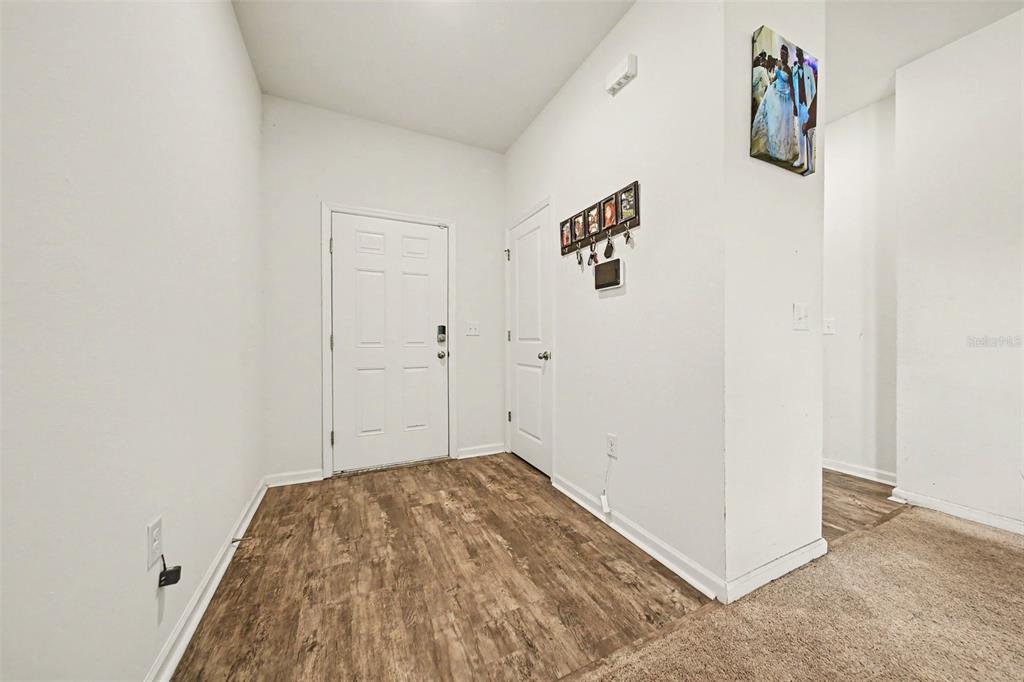 An entryway features wood-look flooring, a white front door, and a wall-mounted key rack — 1006 COMMUTER DR, DELTONA, FL