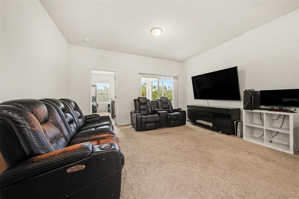 A living room features beige carpet, white walls, black leather furniture, and a large television — 1006 COMMUTER DR, DELTONA, FL