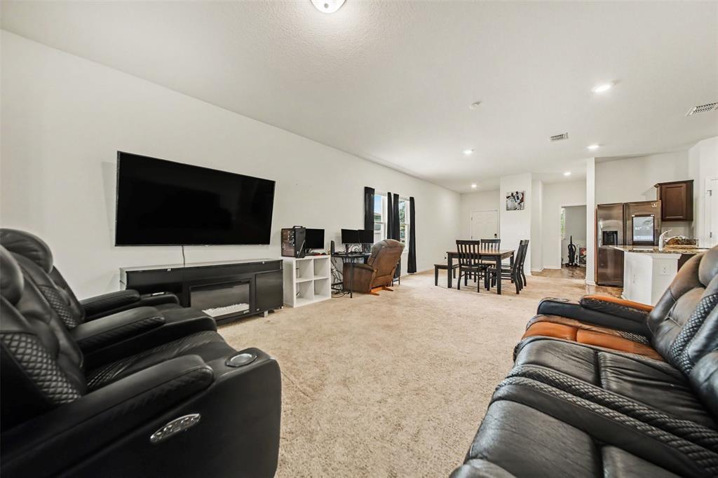 A living room with black leather recliners, a large wall-mounted television, and an adjacent dining area — 1006 COMMUTER DR, DELTONA, FL