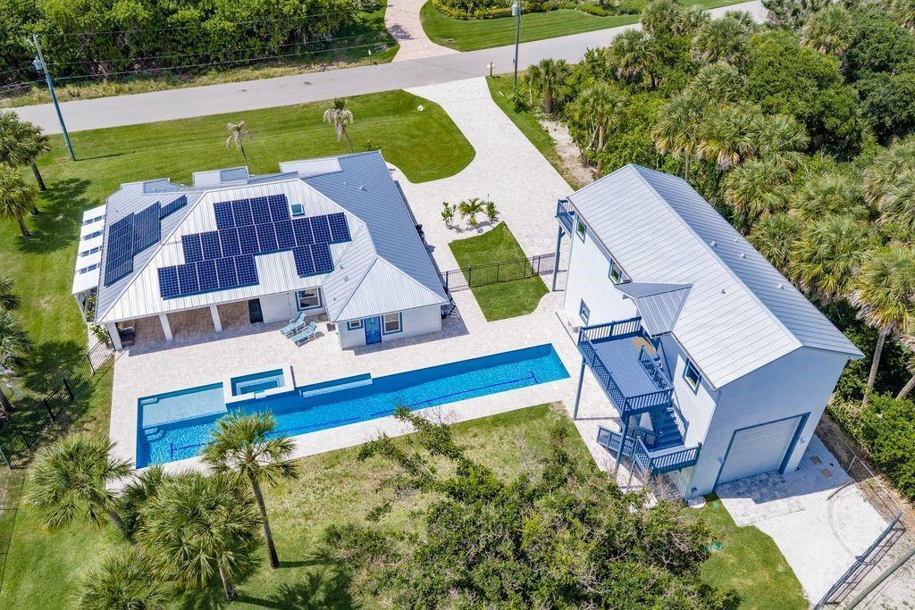 An aerial view shows two white buildings with metal roofs, a long pool, and solar panels — MELBOURNE BEACH, FL