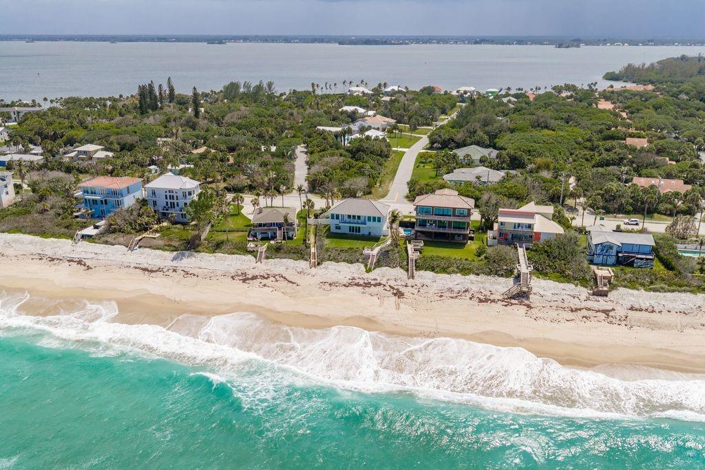 An aerial view shows beachfront houses with wooden stairs leading down to the sandy shore — MELBOURNE BEACH, FL