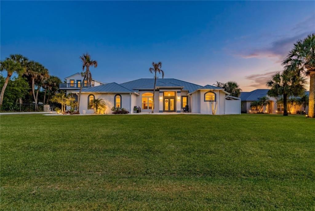 A single-story house with a metal roof and palm trees sits on a large lawn — MELBOURNE BEACH, FL