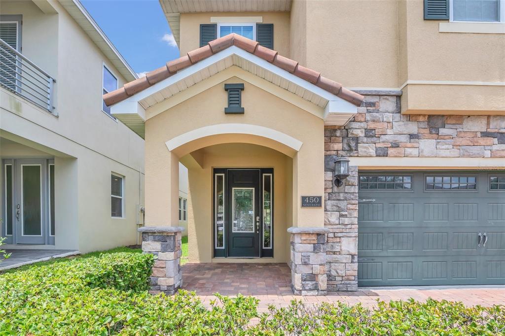 A tan house exterior features a stone-accented entryway, a dark front door, and a garage — 450 NOVI PATH, KISSIMMEE, FL