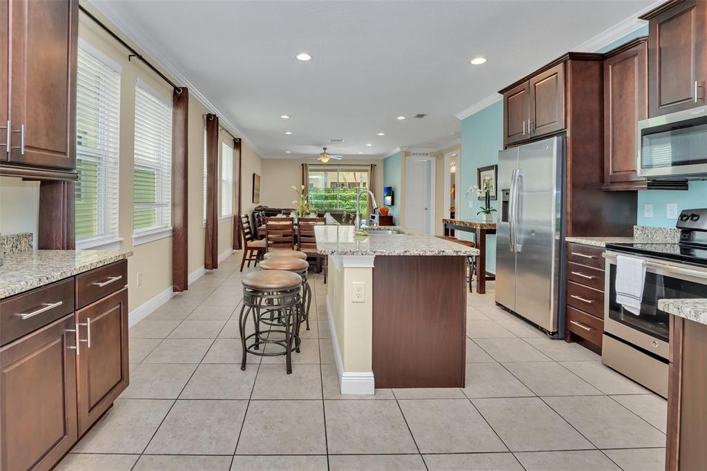 A kitchen with dark wood cabinets, granite countertops, and stainless steel appliances opens to a dining area — 450 NOVI PATH, KISSIMMEE, FL