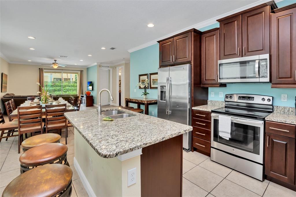 A kitchen with dark wood cabinets, granite countertops, and a central island with bar stools — 450 NOVI PATH, KISSIMMEE, FL