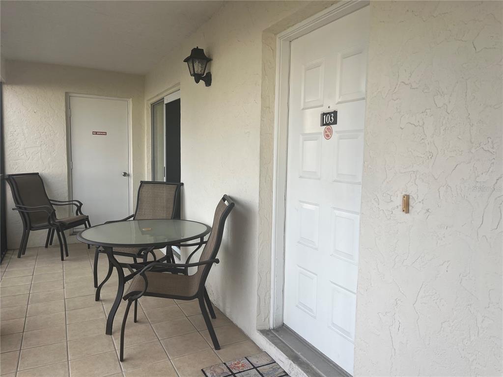 A patio with a table and chairs sits outside a white door numbered 103 — 1531 PLACIDA ROAD UNIT 10-103, ENGLEWOOD, FL