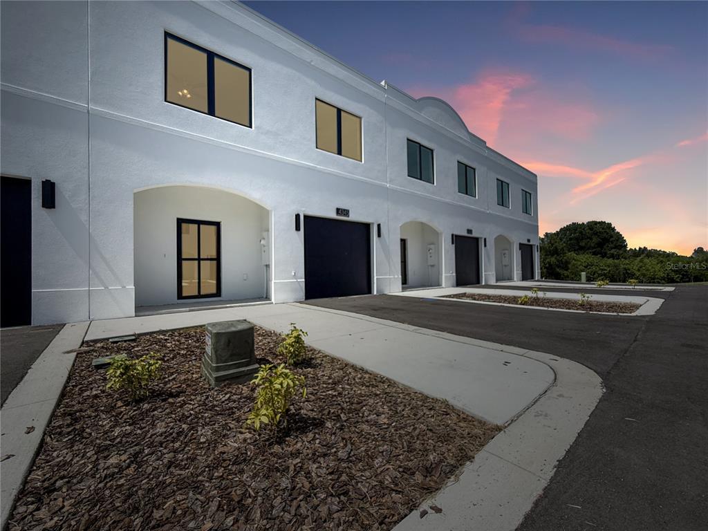 A row of modern white townhomes with dark garage doors and arched entryways at sunset — 4345 CAMBIO GARDENS COURT, TAMPA, FL