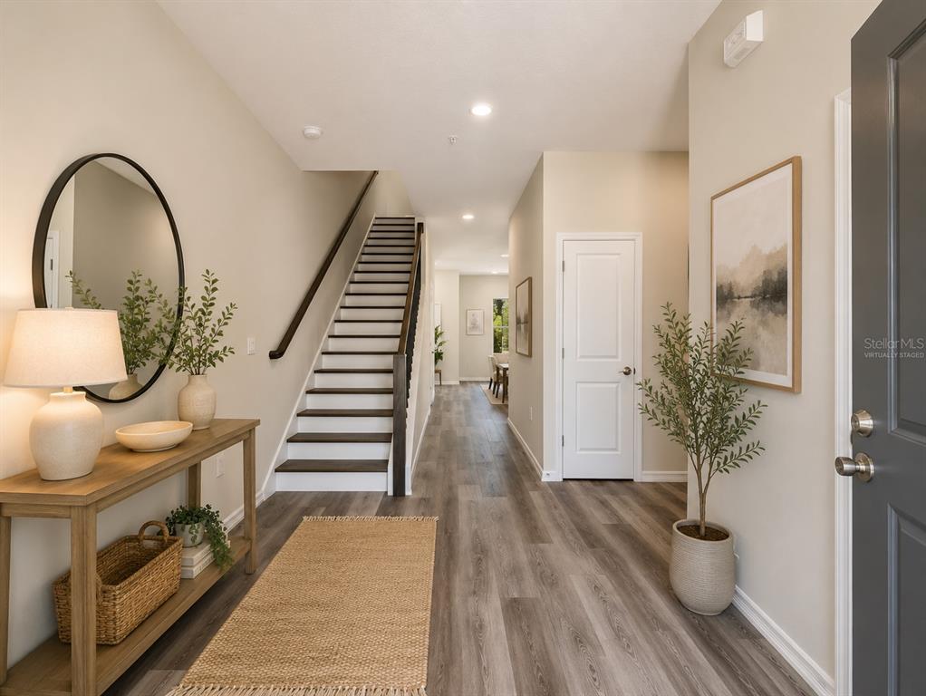 A bright entryway features wood-look flooring, a staircase with dark railings, and a console table — 4345 CAMBIO GARDENS COURT, TAMPA, FL