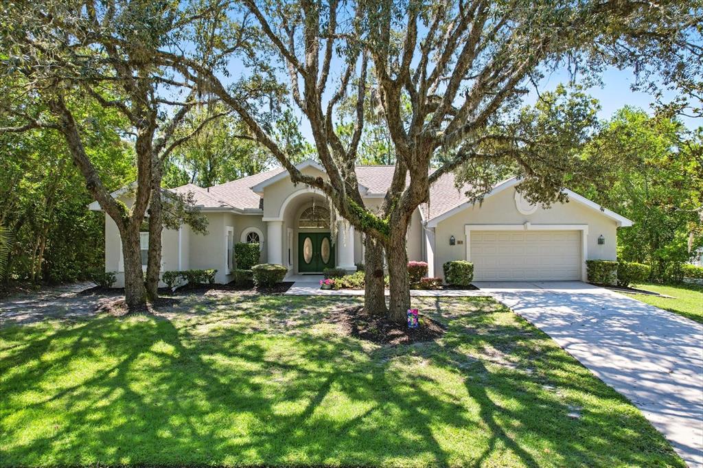 A single-story house with a beige exterior, a two-car garage, and large oak trees — 8 SWEETGUM COURT N, HOMOSASSA, FL