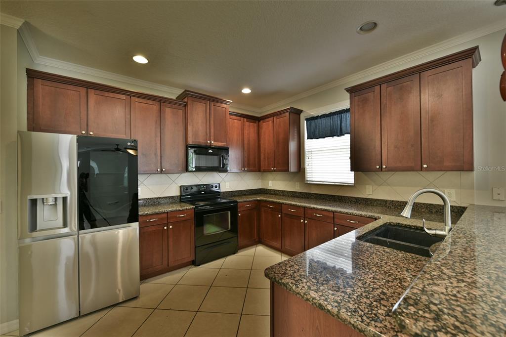 A kitchen featuring dark wood cabinets, granite countertops, stainless steel appliances, and tile flooring — 3341 LAKE JEAN DRIVE, ORLANDO, FL
