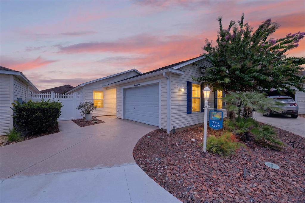 A single-story house with light siding, a garage, and a driveway at sunset — 1813 HORTENSIA PLACE, THE VILLAGES, FL