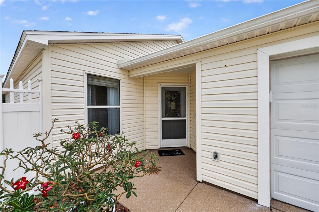 The exterior of a house features beige vinyl siding, a concrete porch, and a front door — 1813 HORTENSIA PLACE, THE VILLAGES, FL