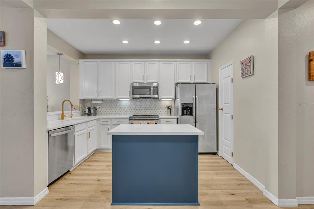 A kitchen features white cabinets, stainless steel appliances, a blue island, and light wood flooring — 995 JUEL STREET, ORLANDO, FL