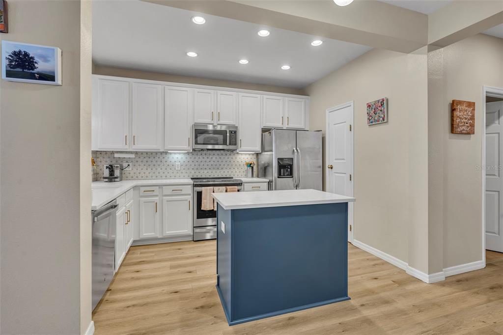A kitchen features white cabinets, stainless steel appliances, a blue island, and light wood flooring — 995 JUEL STREET, ORLANDO, FL