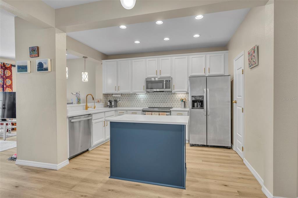 A kitchen features white cabinets, stainless steel appliances, a blue island, and light wood flooring — 995 JUEL STREET, ORLANDO, FL