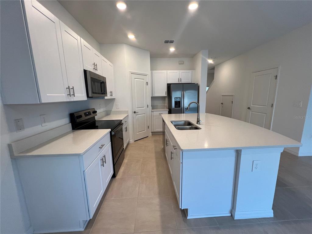 A modern kitchen features white cabinets, quartz countertops, a large island, and black appliances — 2211 PORTRAIT STREET, KISSIMMEE, FL