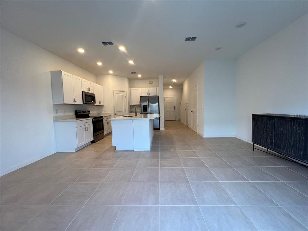 A kitchen with white cabinets, stainless steel appliances, and a central island on tiled flooring — 2211 PORTRAIT STREET, KISSIMMEE, FL