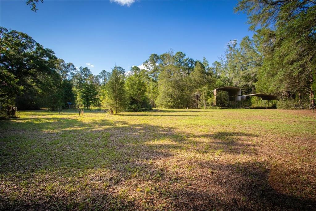 A grassy, open lot features a metal carport structure surrounded by mature trees — 11418 NW 161ST STREET, ALACHUA, FL