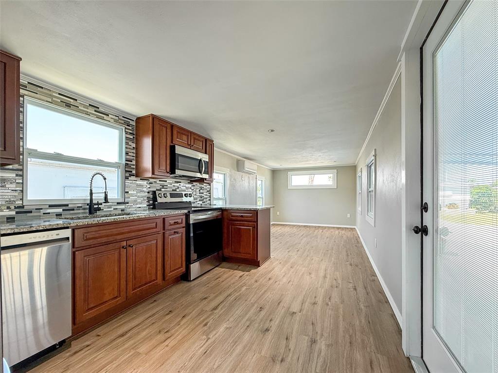 A kitchen with wood cabinets, stainless steel appliances, and light wood flooring opens to a room — 5141 OAKLAND HILLS AVENUE, SARASOTA, FL