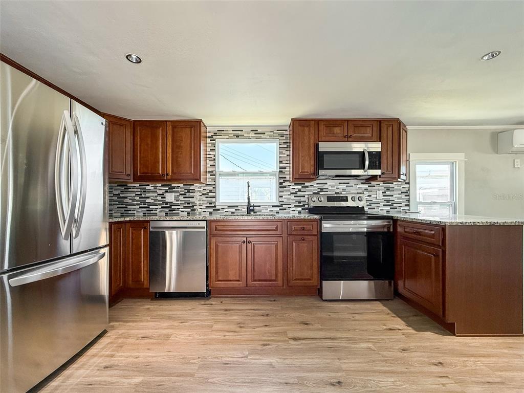 A kitchen features wood cabinets, stainless steel appliances, a tiled backsplash, and light wood flooring — 5141 OAKLAND HILLS AVENUE, SARASOTA, FL
