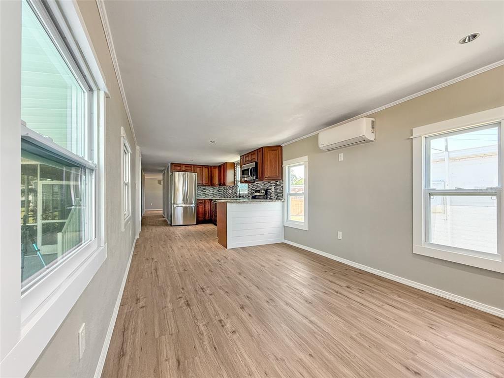 An open-concept living area with wood-look flooring, a kitchen with dark cabinets, and wall-mounted AC — 5141 OAKLAND HILLS AVENUE, SARASOTA, FL