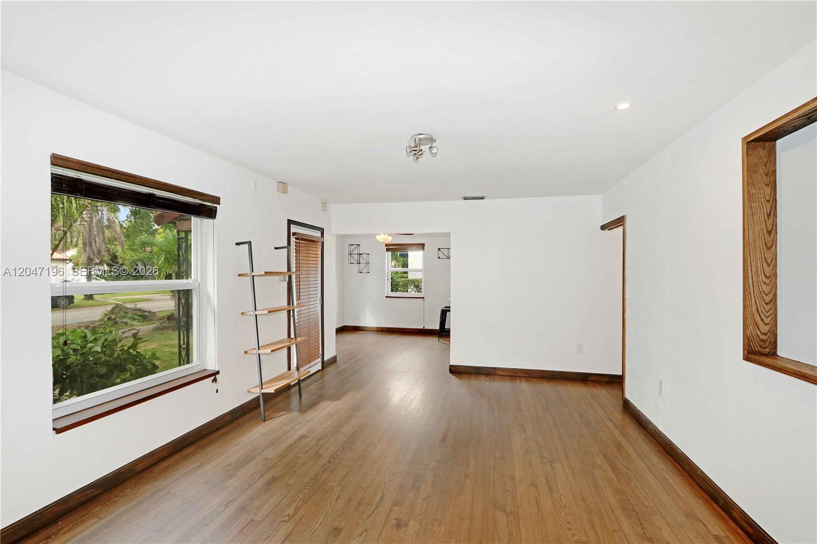 An empty living room features hardwood floors, white walls, and a wooden shelving unit — 221 Camilo Ave, Coral Gables FL 33134, CORAL GABLES, FL