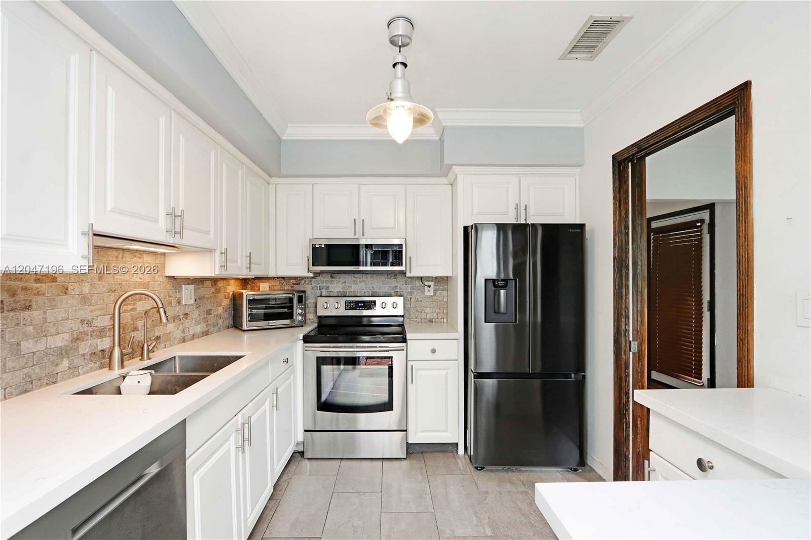 A kitchen features white cabinetry, stainless steel appliances, a black refrigerator, and a stone backsplash — 221 Camilo Ave, Coral Gables FL 33134, CORAL GABLES, FL