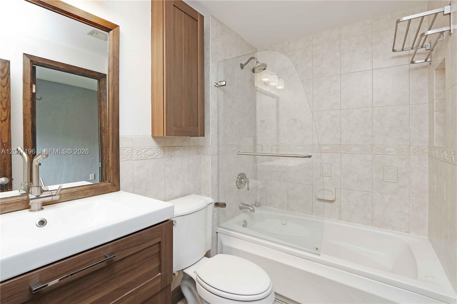 A bathroom features a wood vanity, a toilet, and a bathtub with a glass shower panel — 221 Camilo Ave, Coral Gables FL 33134, CORAL GABLES, FL