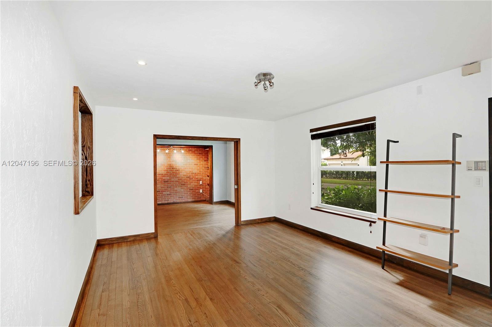 A room with hardwood floors, white walls, a brick-accented doorway, and a leaning bookshelf — 221 Camilo Ave, Coral Gables FL 33134, CORAL GABLES, FL