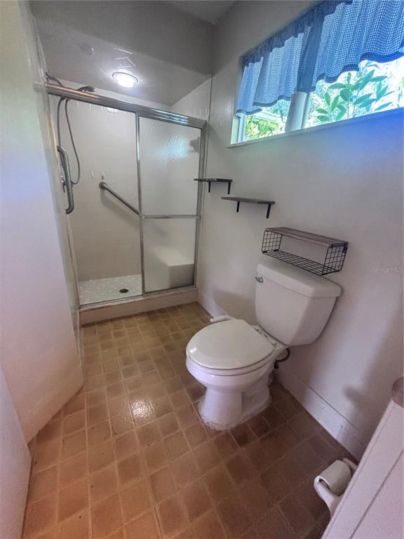 A bathroom features a walk-in shower with sliding glass doors, a toilet, and wall shelving — 8947 SW 108TH PLACE, OCALA, FL
