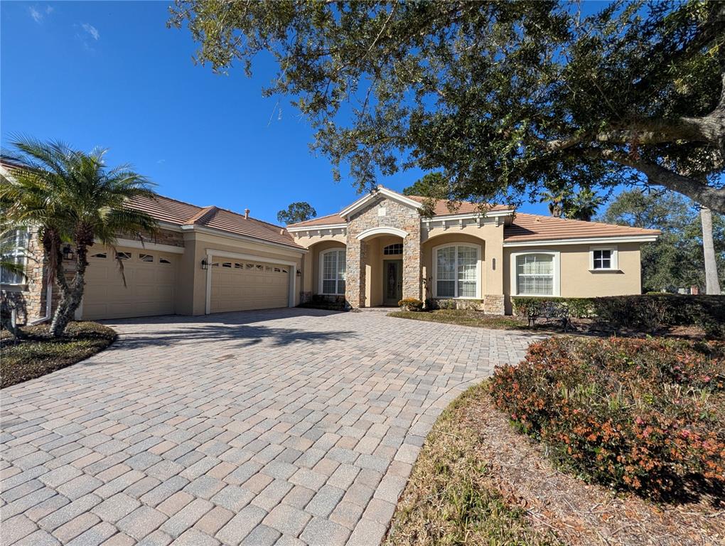 A single-story house with a stone-accented facade, a paver driveway, and a three-car garage — 8492 DUNHAM STATION DRIVE, TAMPA, FL